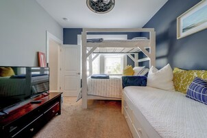 Un dormitorio con una litera, un televisor sobre un mueble de madera y una puerta que da a otra habitación.