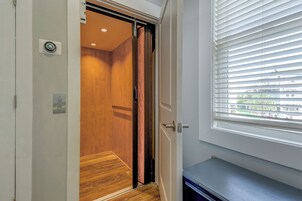 Una habitación con suelo de madera, una puerta con picaporte, una ventana con persianas y una mesita.
