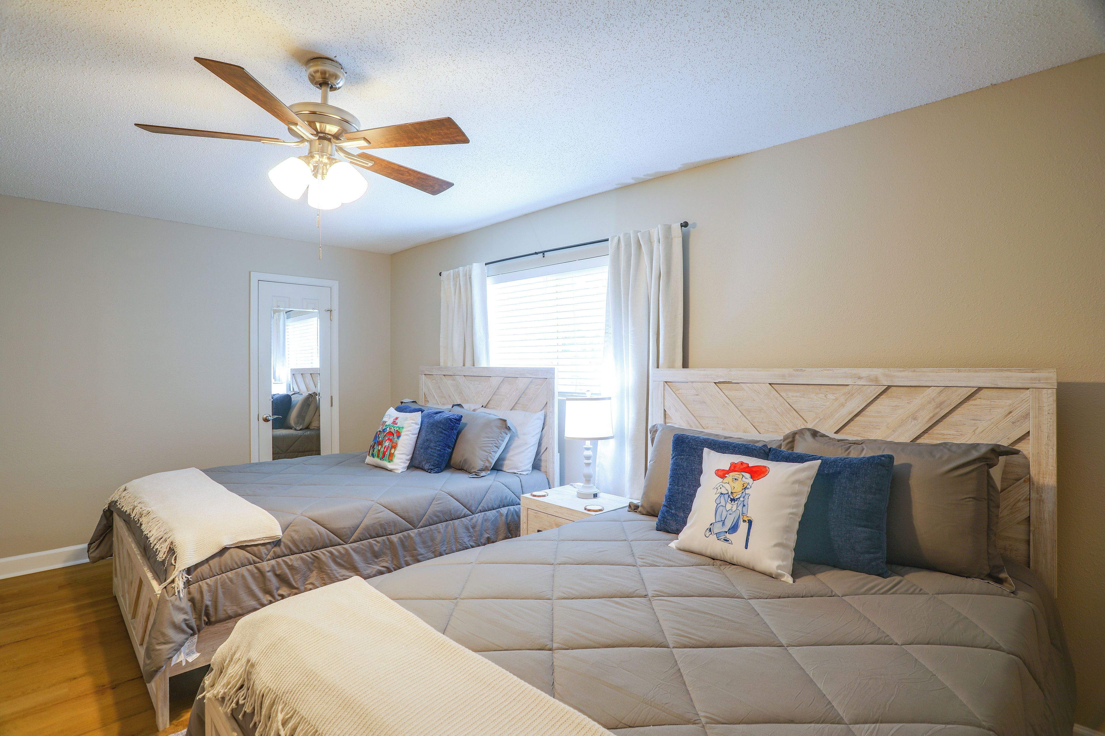 A bedroom with two beds, a ceiling fan, a window with blinds, and a door.