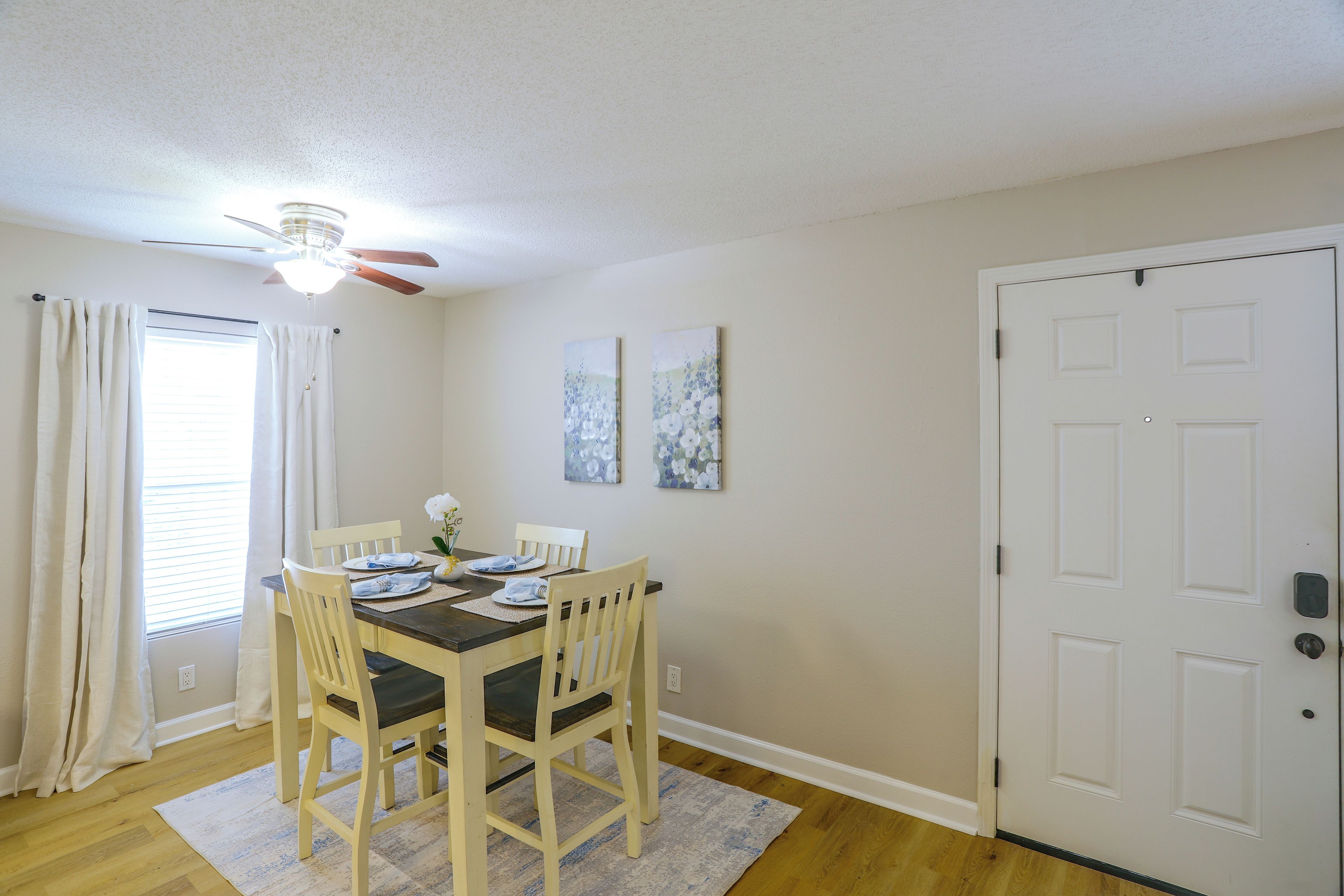 A dining area with a table set for four, a ceiling fan, and a door to the right.