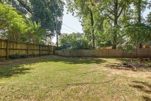 A backyard with a wooden fence, a grassy lawn, and trees. - Near Midtown Attractions! Memphis Duplex (Memphis)