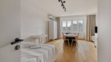 A hotel room with a bed, a desk, a chair, a TV, and a window with a city view.