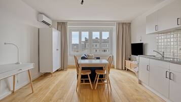 A modern kitchen with a dining area, wooden flooring, and a view of buildings through large windows.