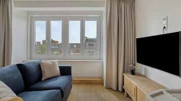 A modern living room with a large window, a flat-screen TV, a wooden cabinet, and a blue sofa.
