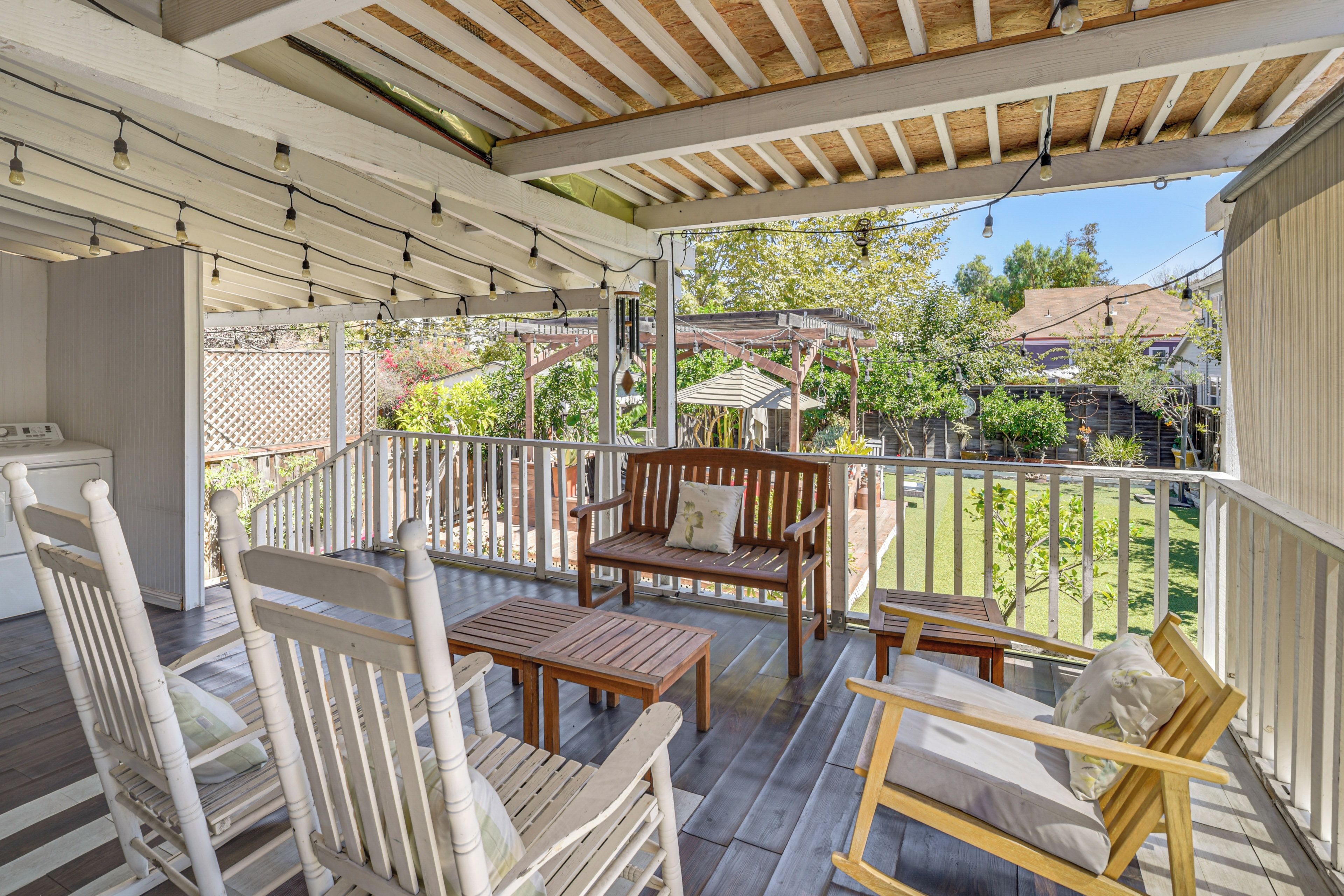 A covered patio with wooden furniture, a white railing, and a view of a residential area.