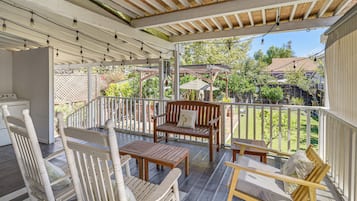 A covered patio with wooden furniture, a white railing, and a view of a residential area.