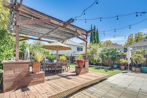 Eine Holzterrasse mit Gartenmöbeln, Lichterketten und Blumentöpfen.