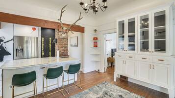 A kitchen with a central island, bar stools, a chandelier, and a cabinet with glass doors.