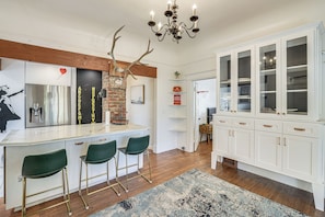 A kitchen with a central island, bar stools, a chandelier, and a cabinet with glass doors.
