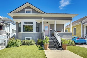 Ein zweistöckiges Wohnhaus mit einer Veranda, einer Treppe, die zum Eingang führt, und einem kleinen Gartenbereich mit Topfpflanzen.