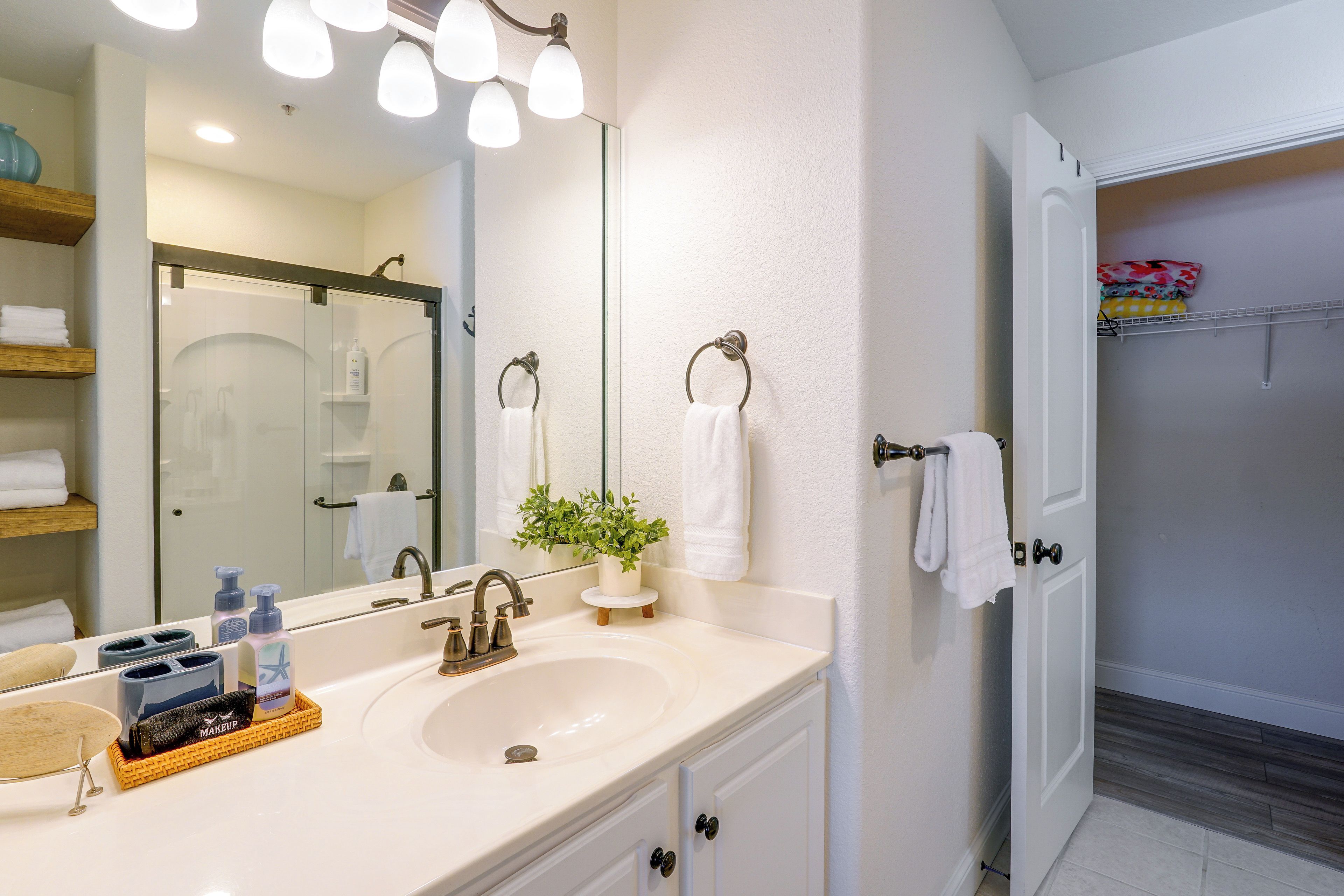 A bathroom with a white sink, a mirror, a potted plant, and a towel rack.