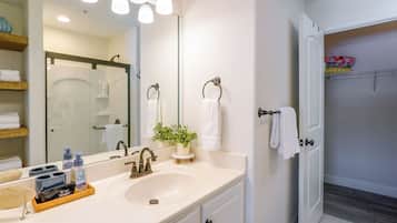 A bathroom with a white sink, a mirror, a potted plant, and a towel rack.