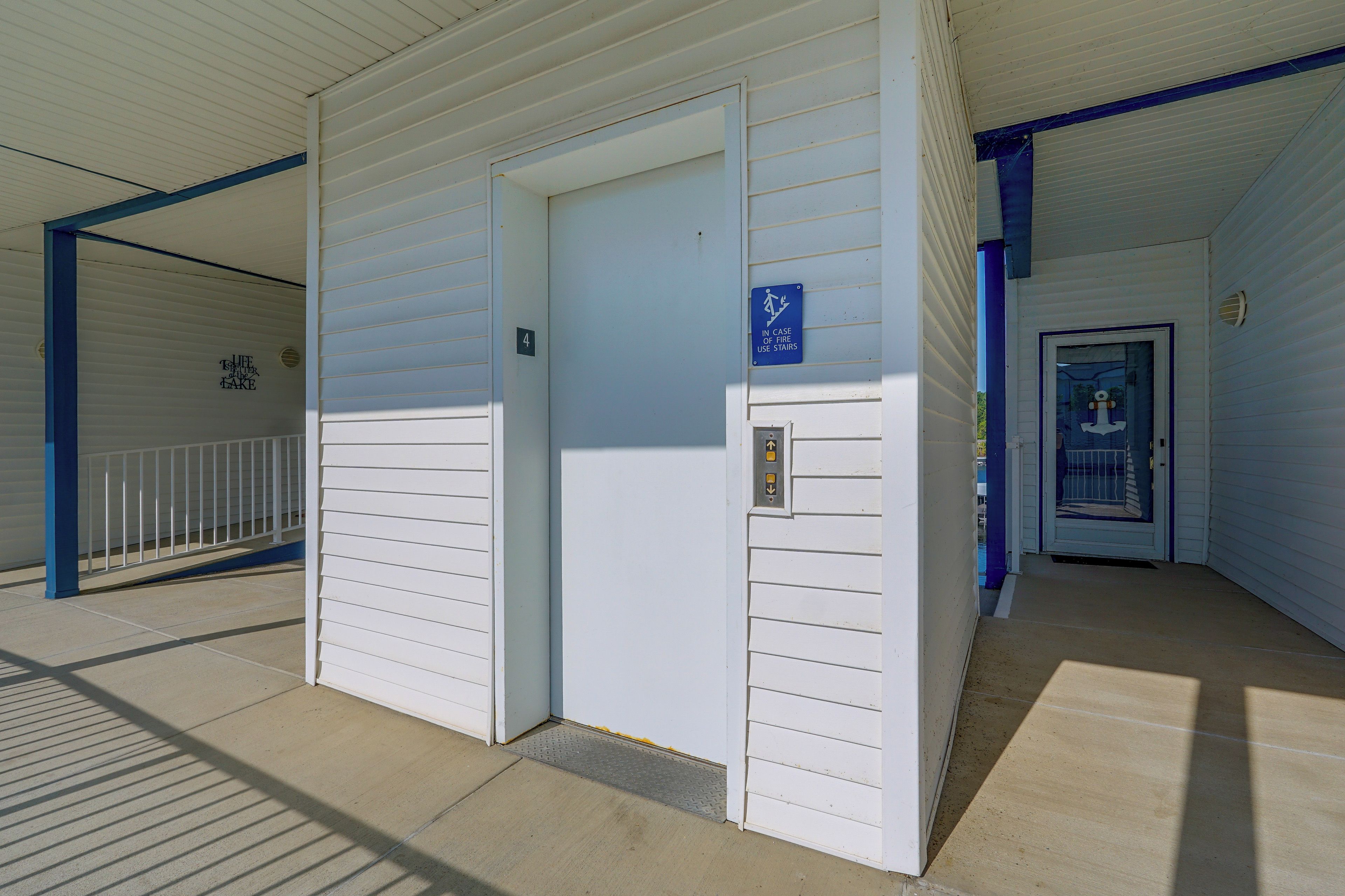 Entrada de un edificio con un letrero de salida de emergencia azul, una puerta con placa de número y una puerta metálica de acceso a una escalera.