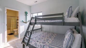 A bunk bed with a nautical-themed bedding, a window with a view, and a bathroom with a striped shower curtain.