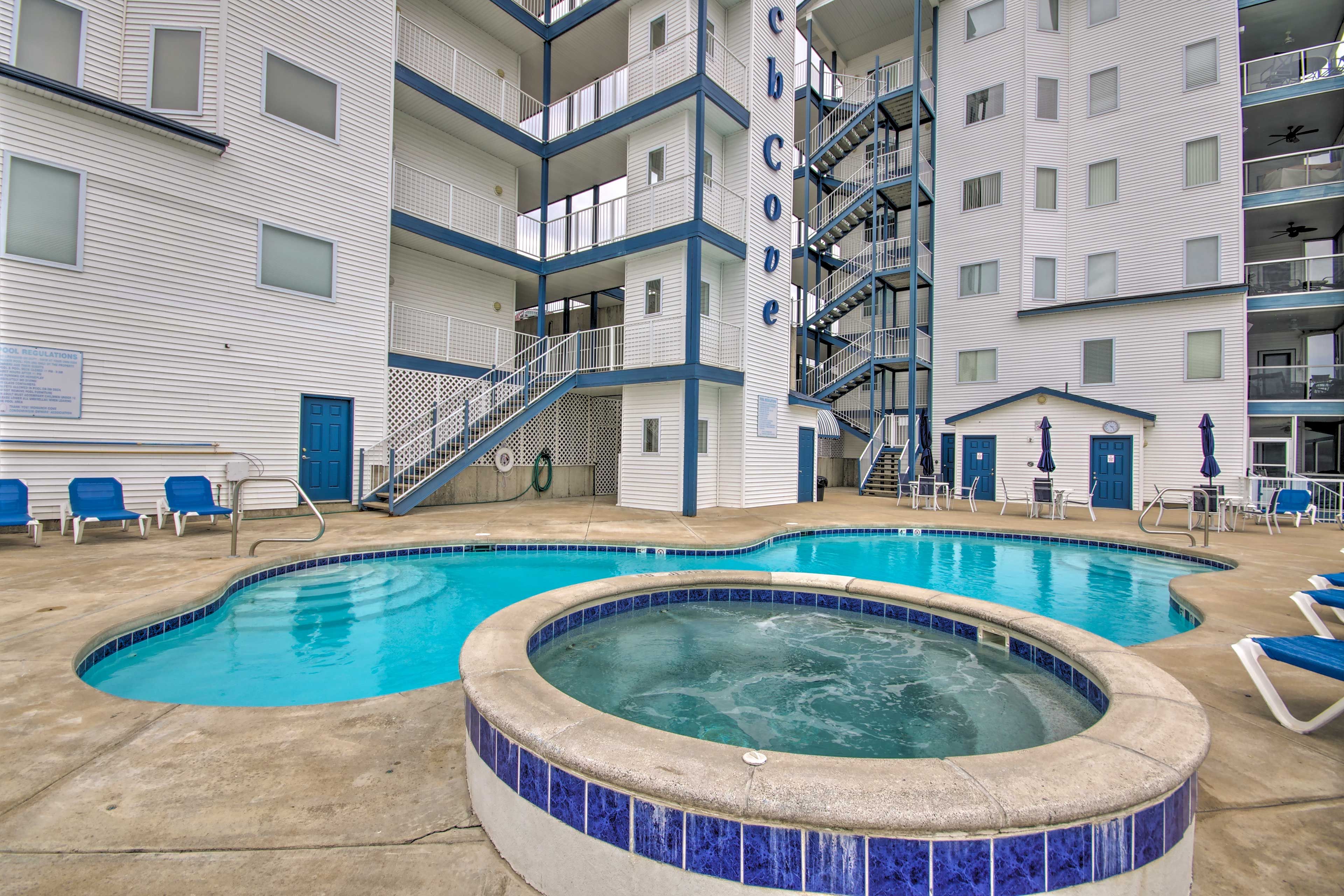 A pool area with a hot tub and lounge chairs, surrounded by a multi-story building with balconies.