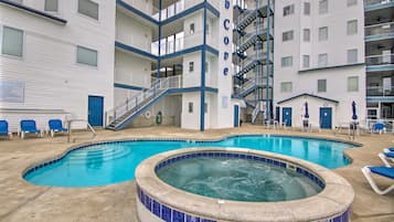 A pool area with a hot tub and lounge chairs, surrounded by a multi-story building with balconies.
