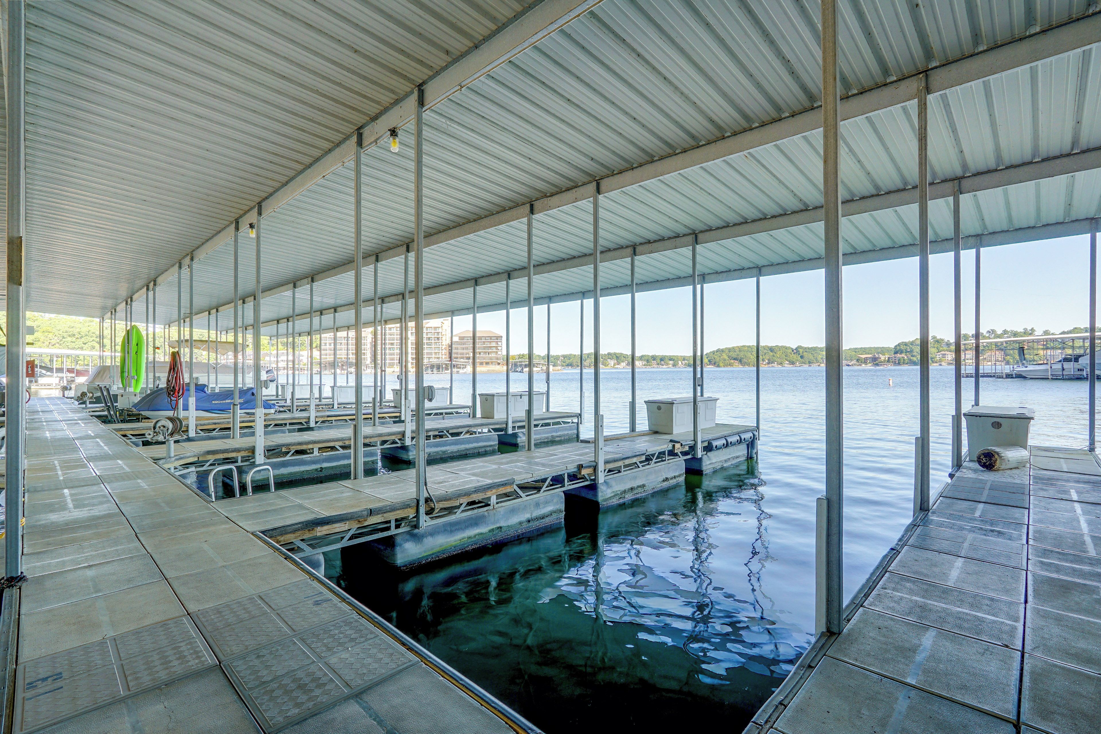 A covered swimming area with multiple docks extending into the water, a green surfboard, and a view of buildings across the water.