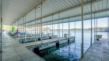 A covered swimming area with multiple docks extending into the water, a green surfboard, and a view of buildings across the water.