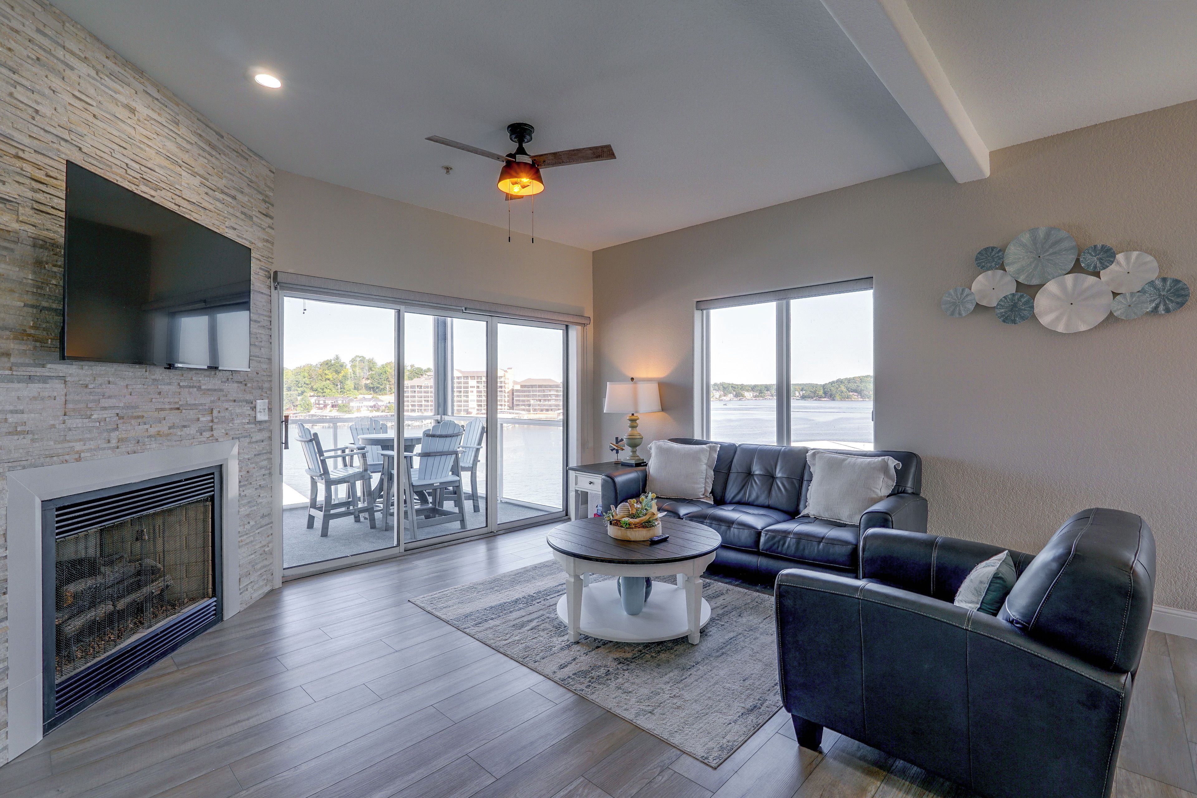 A modern living room with a fireplace, a ceiling fan, and a view of the outdoors through large windows.