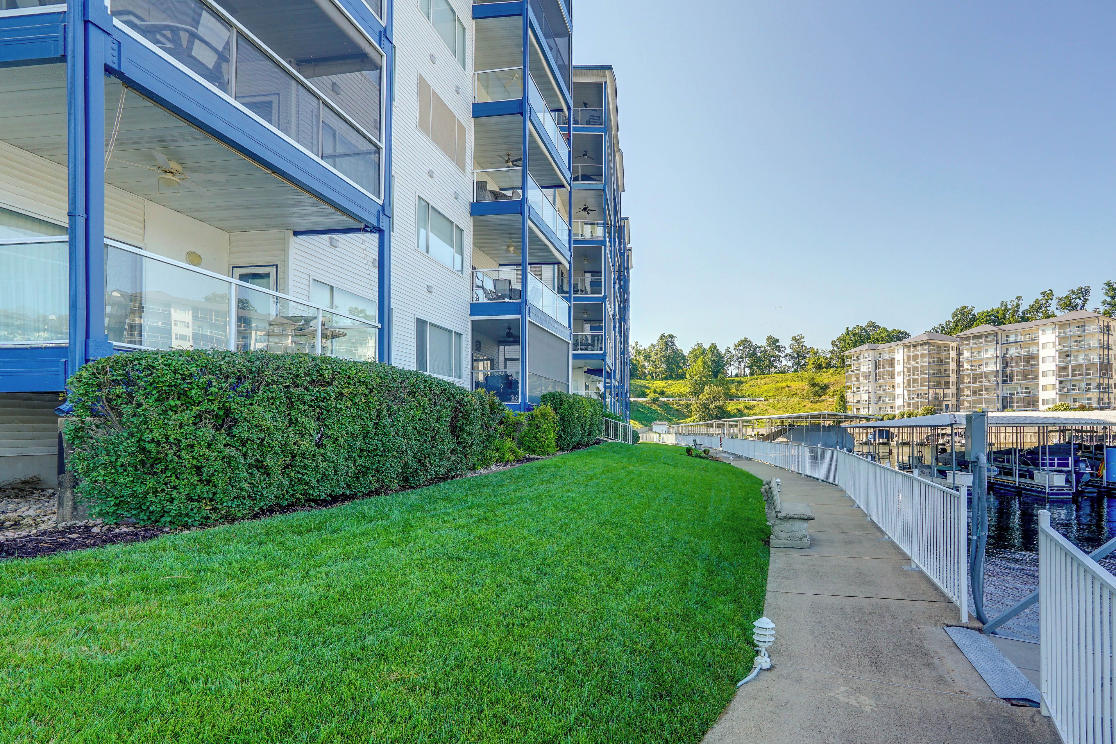 A modern apartment building with balconies, a well-maintained lawn, and a dock area with boats.