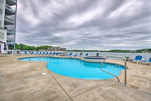 A swimming pool with blue chairs, a metal pool ladder, and a view of a building and trees in the background. - Pool Access! Family Getaway on Lake of the Ozarks (Lake Ozark)