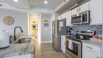 A modern kitchen with stainless steel appliances, a marble countertop, and a view into the dining area.