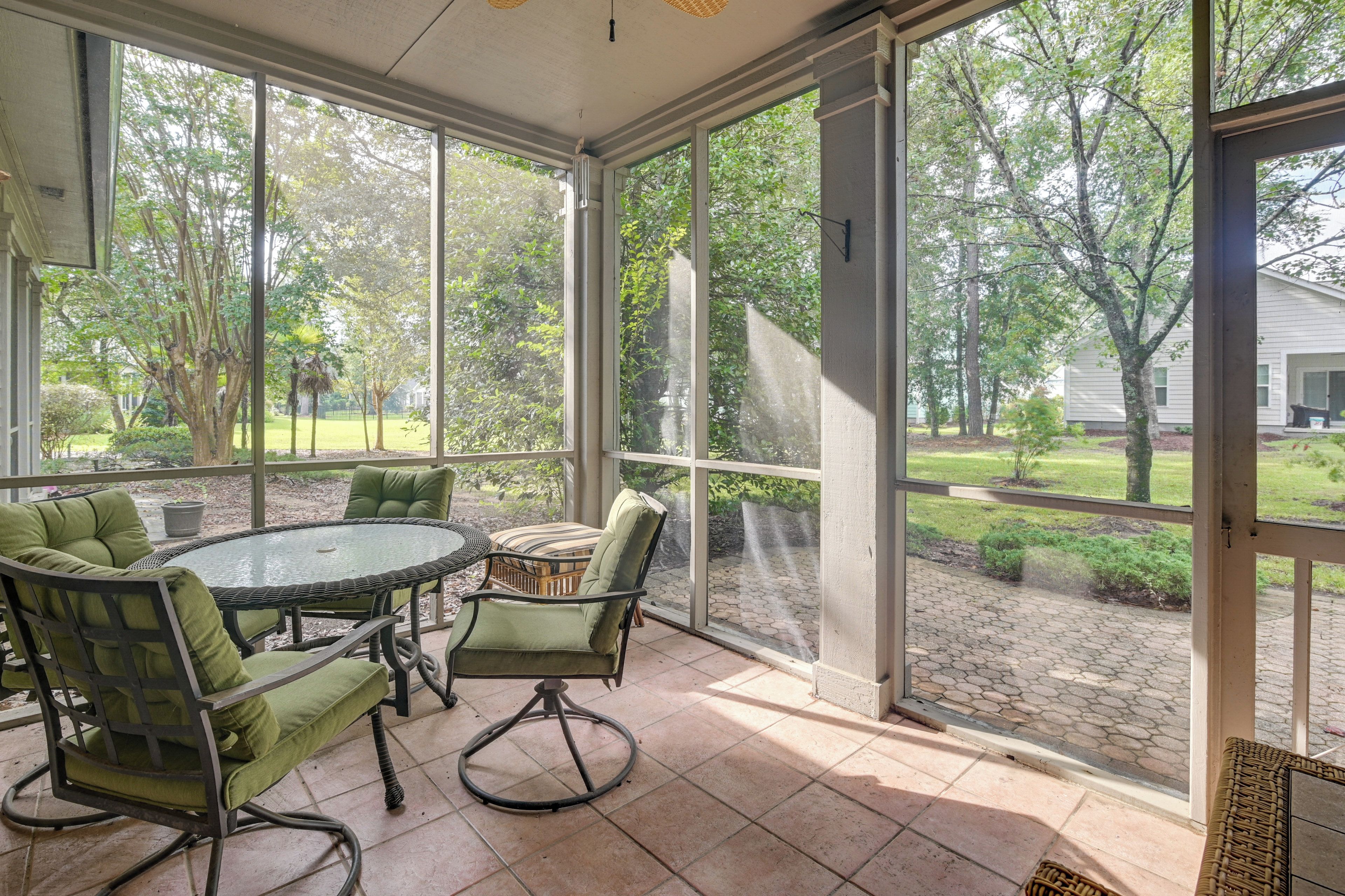 A covered patio with a round table and chairs, large windows, and a view of a garden.