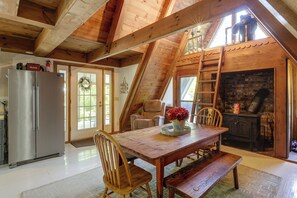 A rustic kitchen with a wooden ceiling, a refrigerator, a dining table with chairs, and a fireplace.