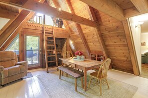 A cozy attic room with a wooden table, chairs, a ladder, and a fireplace.