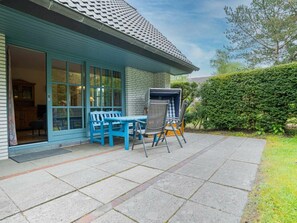 A patio with a table and chairs, a grill, and a blue door leading to an interior space. - Ground Floor in the Reimer House (St. Peter-Ording)