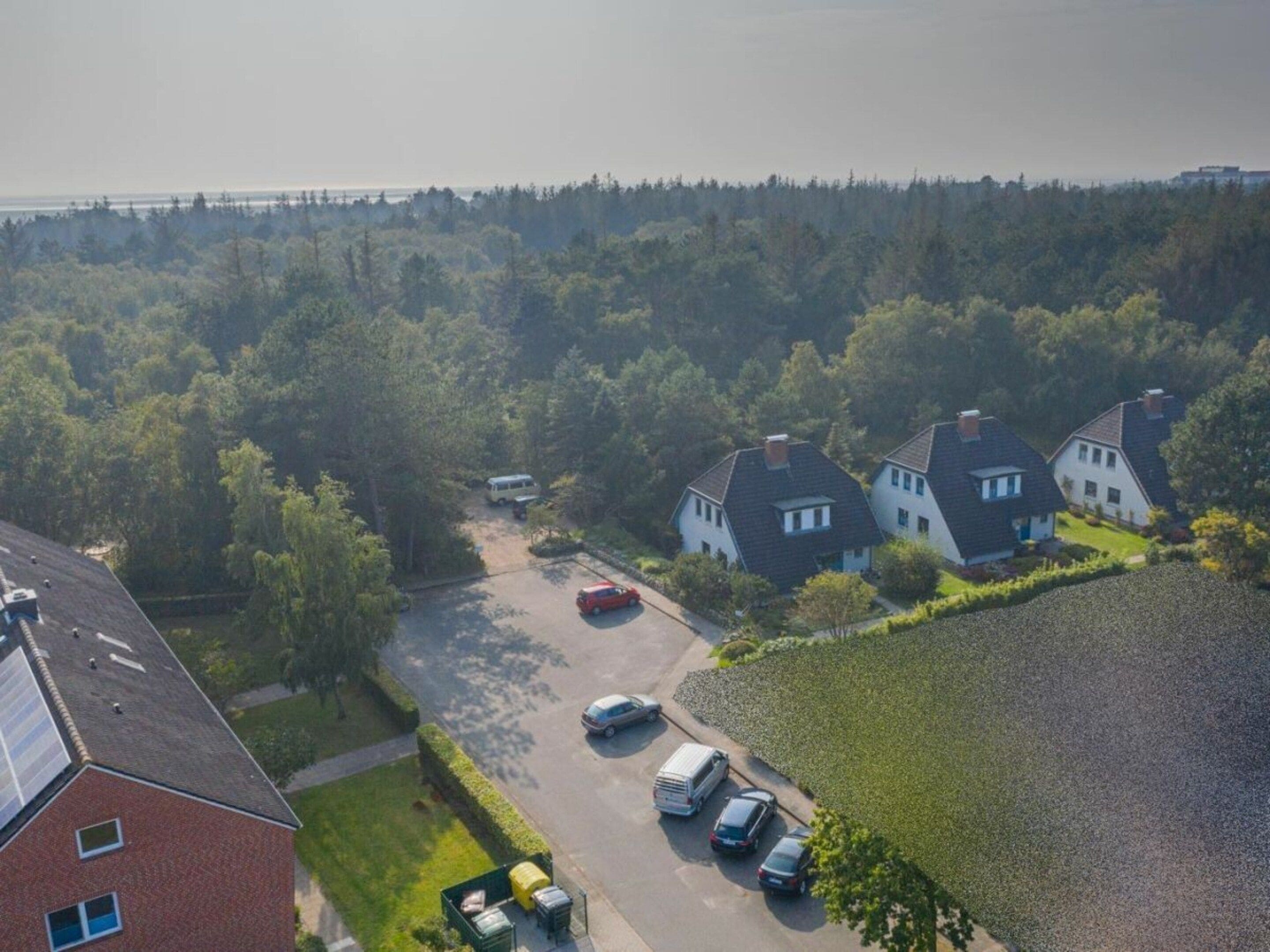 A residential area with detached houses, a parking lot, and a body of water in the background.