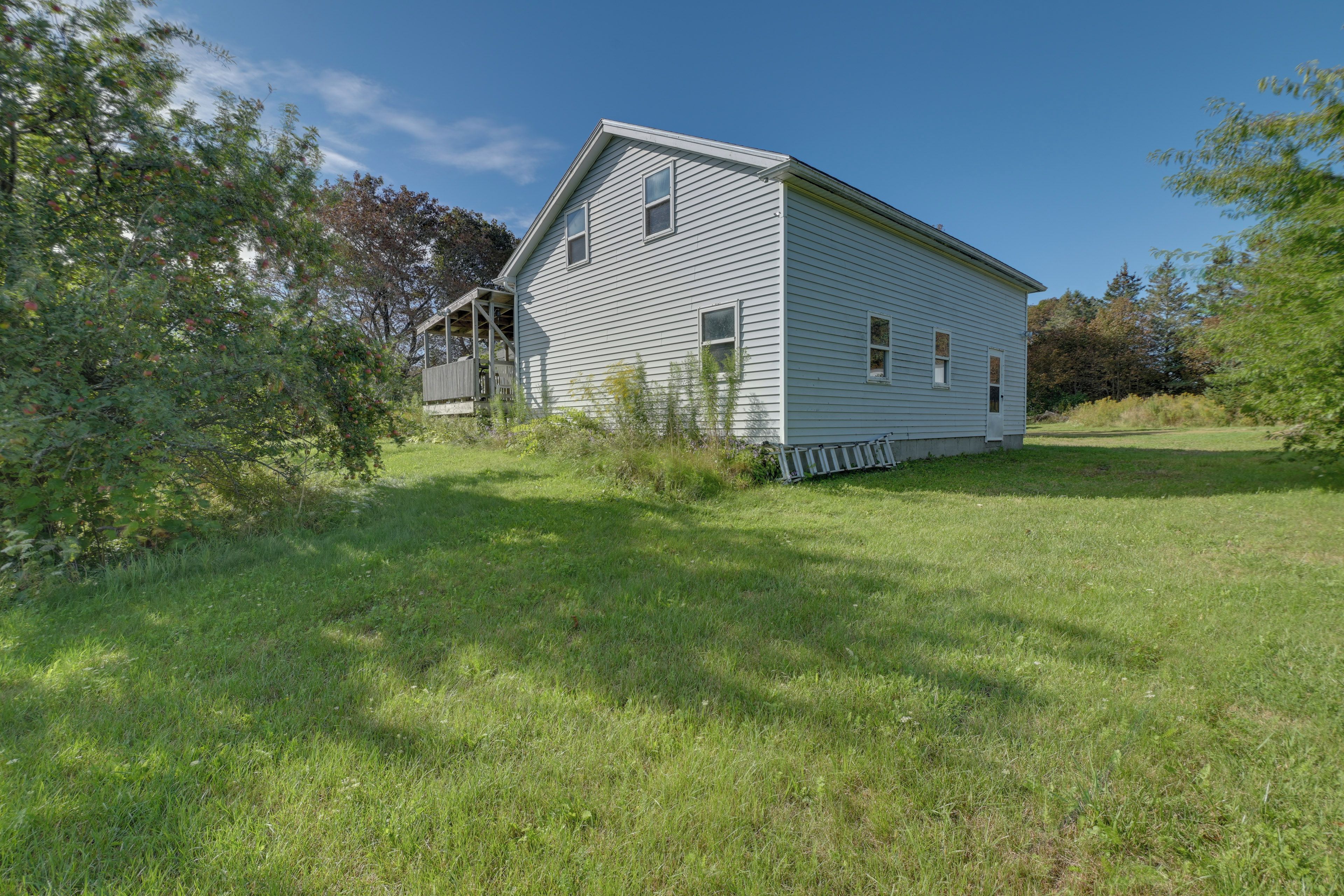 A single-story house with a porch, surrounded by grass and trees.