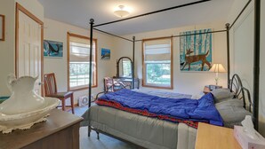 A bedroom with a four-poster bed, a desk with a chair, a dresser, and a window with a view of trees.