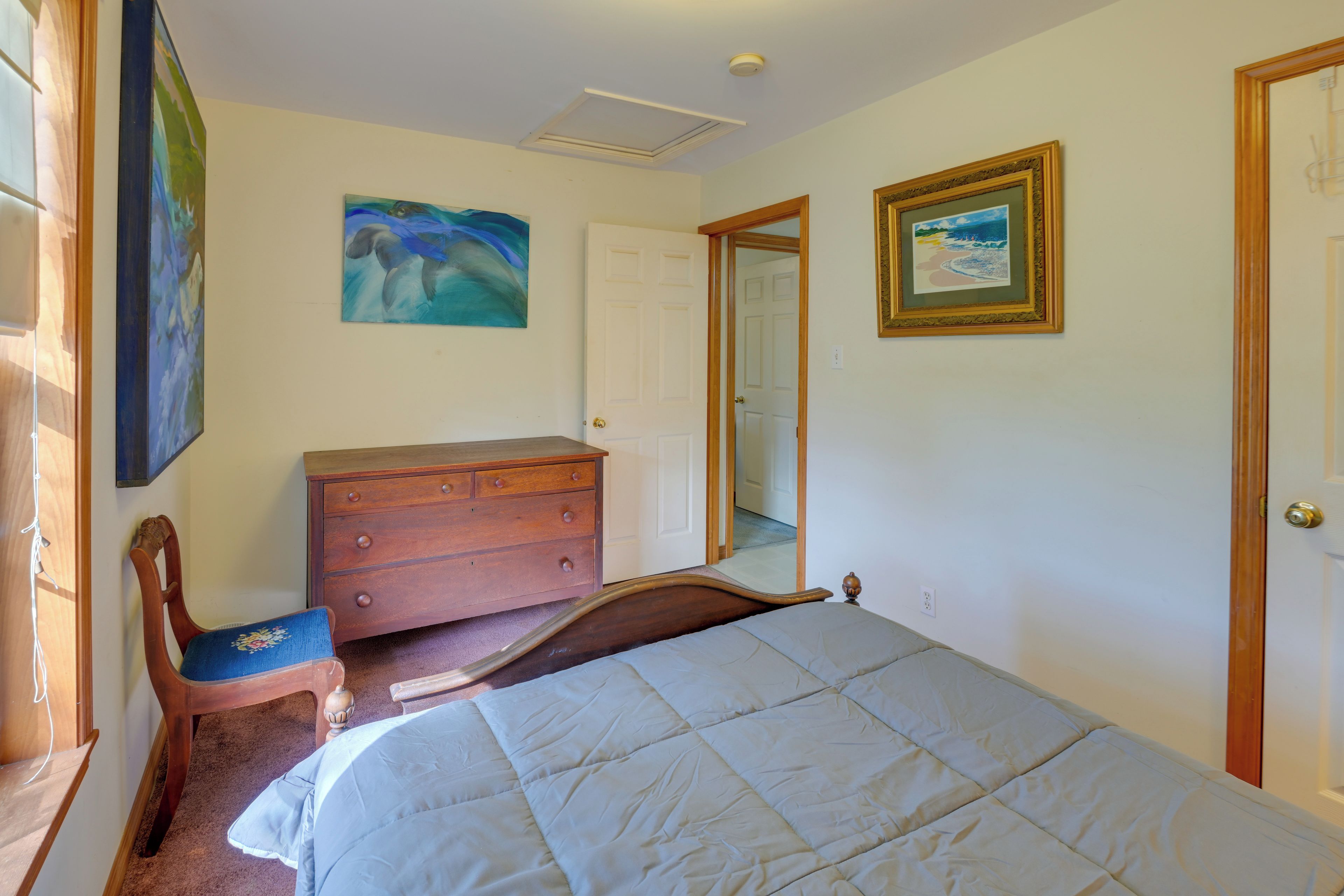 Quarto com cama, penteadeira, cadeira e duas pinturas na parede.