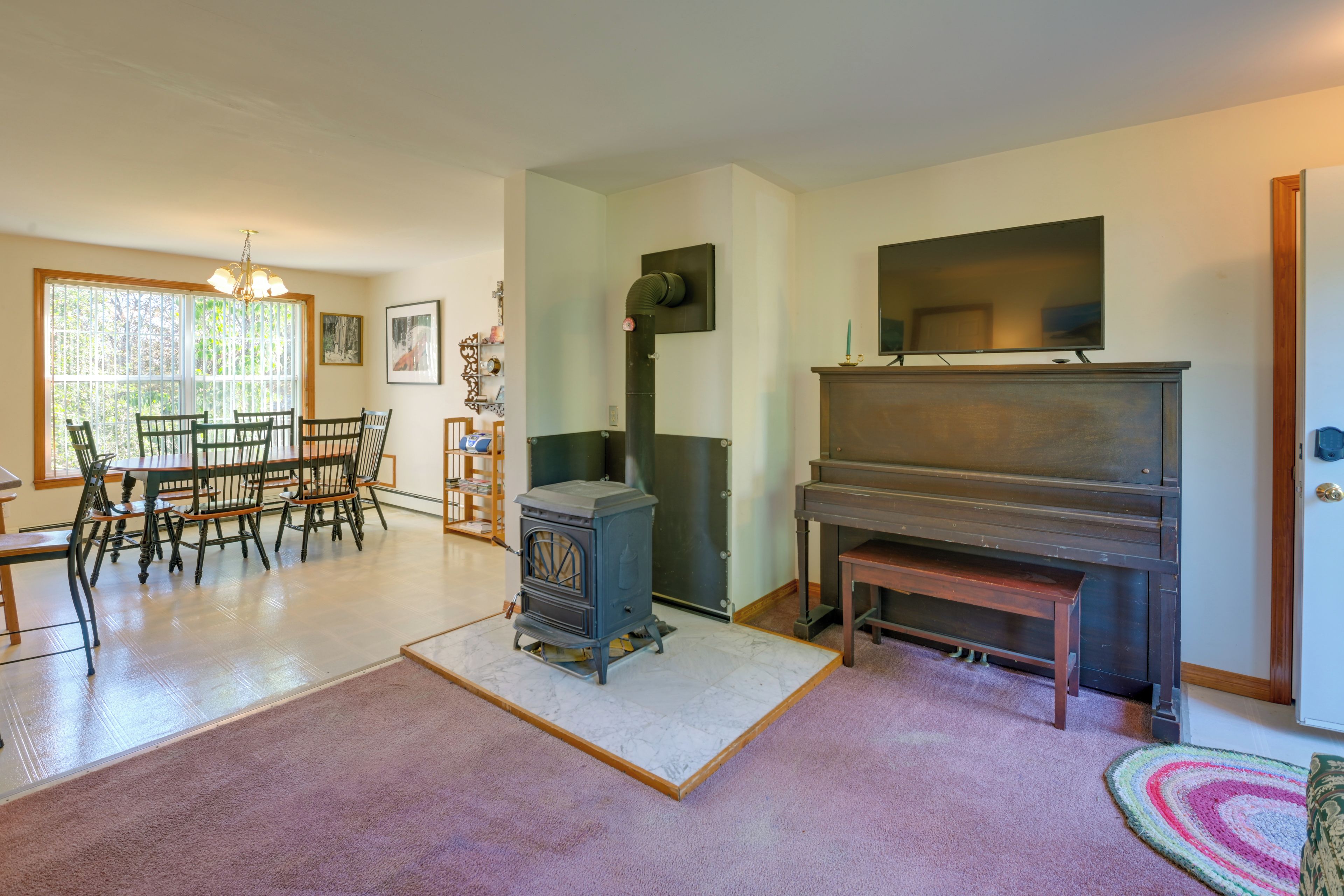 Una sala de estar con chimenea, un comedor con sillas, un televisor y un ventanal grande.