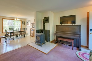 A living room with a fireplace, a dining area with chairs, a television, and a large window. - 21 Acres, Near Trails to Shore With Island Access (Lubec)
