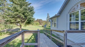 A wooden deck leading to a house with a satellite dish and a large tree in the background.