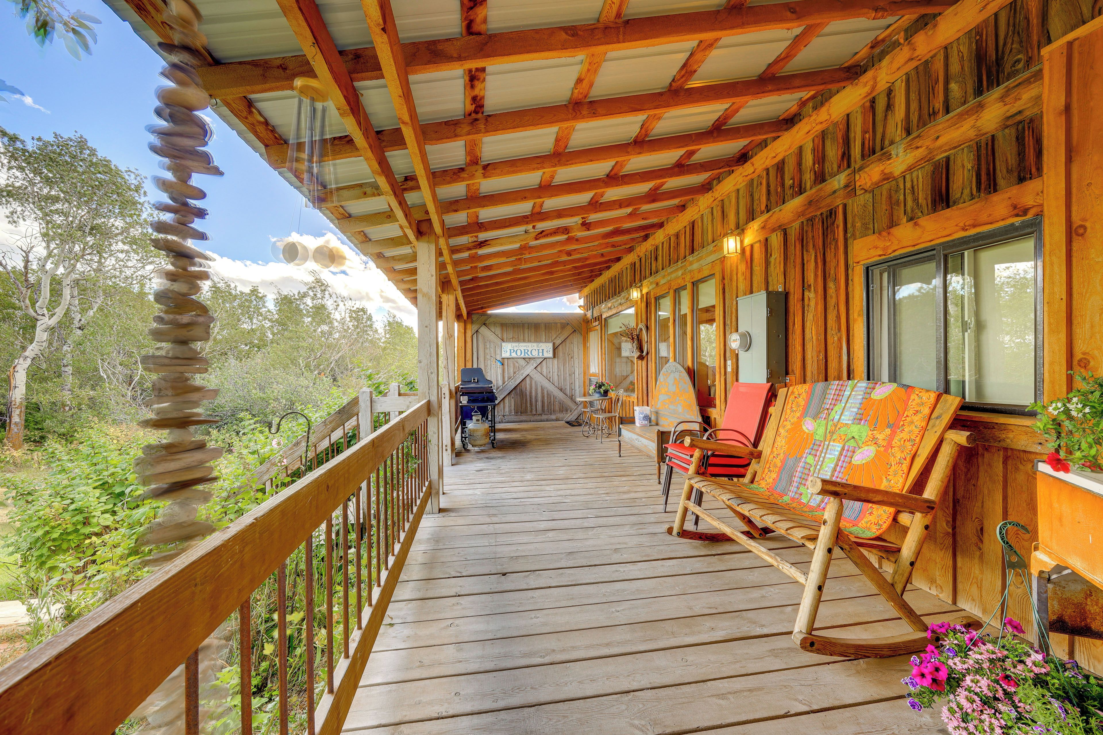 A wooden porch with a railing, a barbecue grill, and a bench.