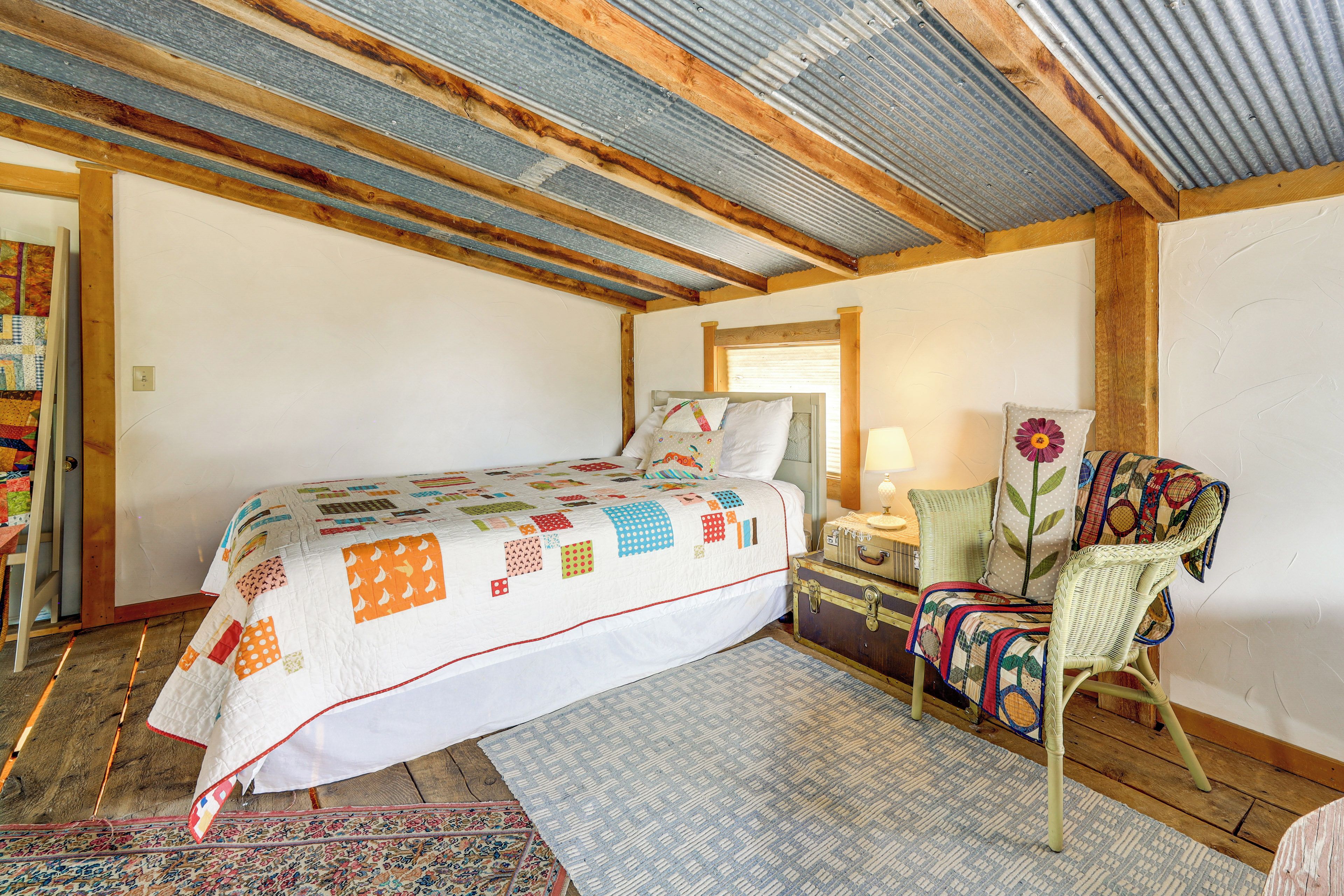 A bedroom with a bed, a chair, a rug, and a window.