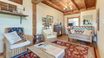 A cozy living room with a wooden ceiling, a sofa, two armchairs, a coffee table, and a rug.