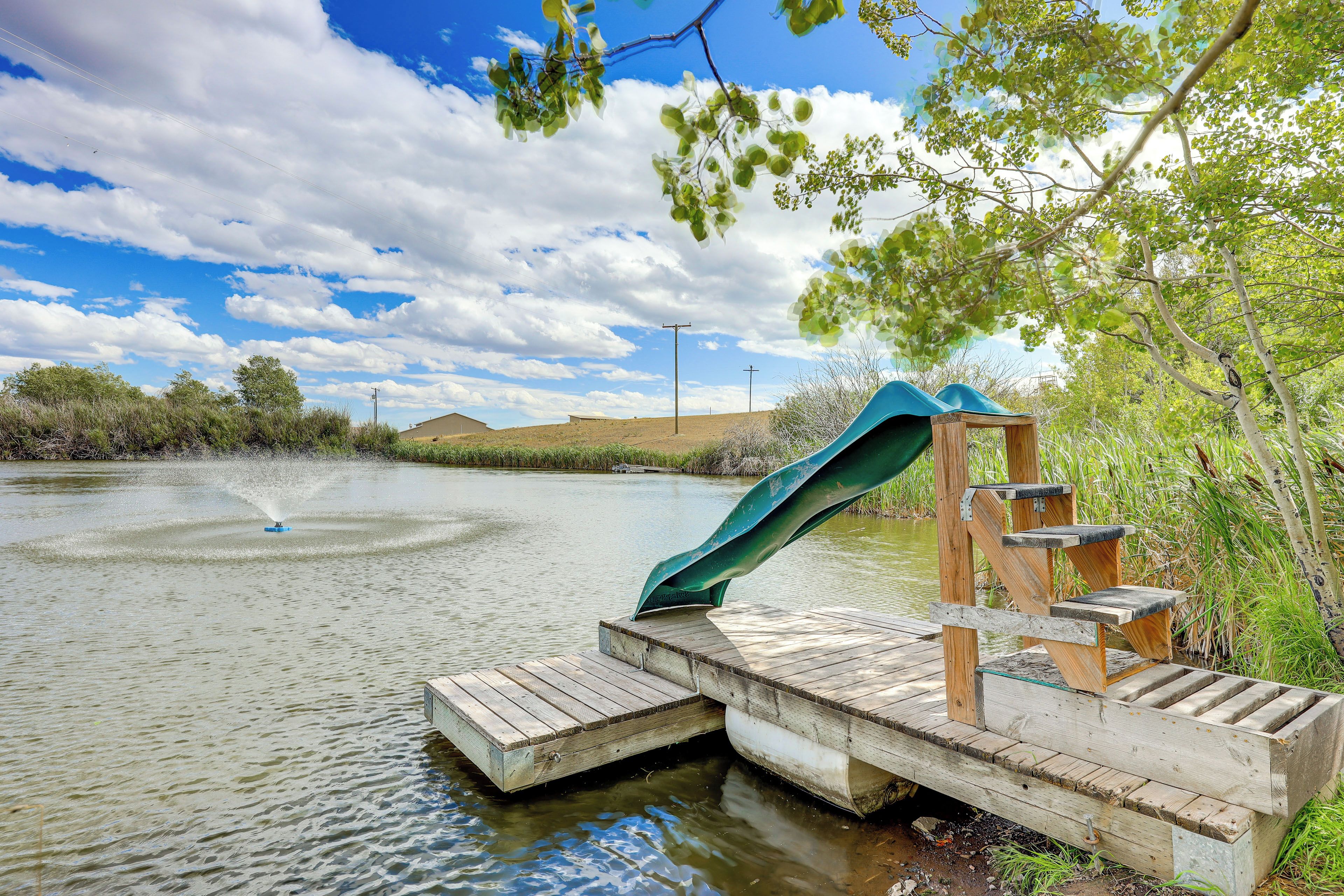 A wooden dock extending into a body of water with a green slide and steps.