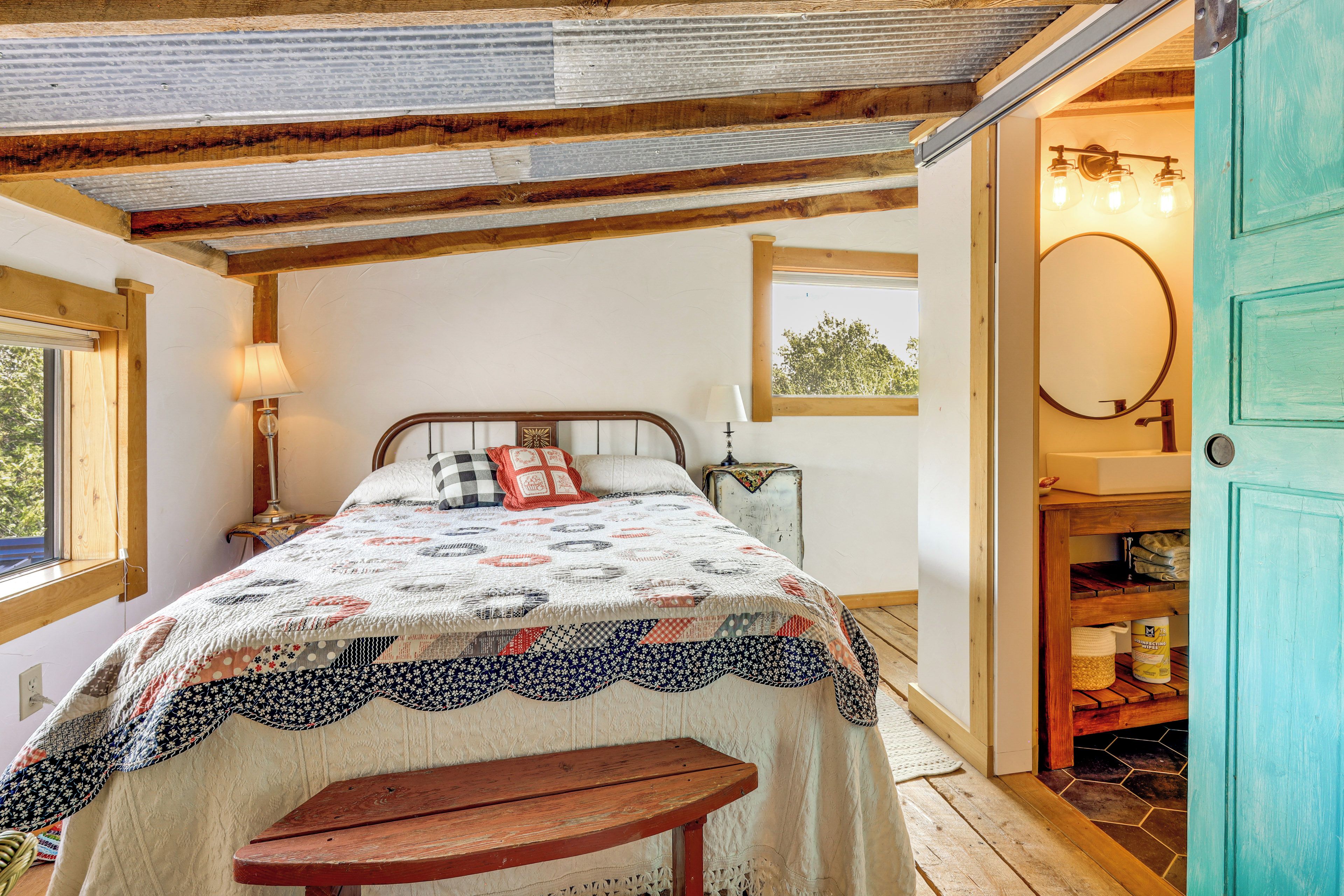 Een slaapkamer met een bed, een bankje, een raam, een lamp, een spiegel en een deur.