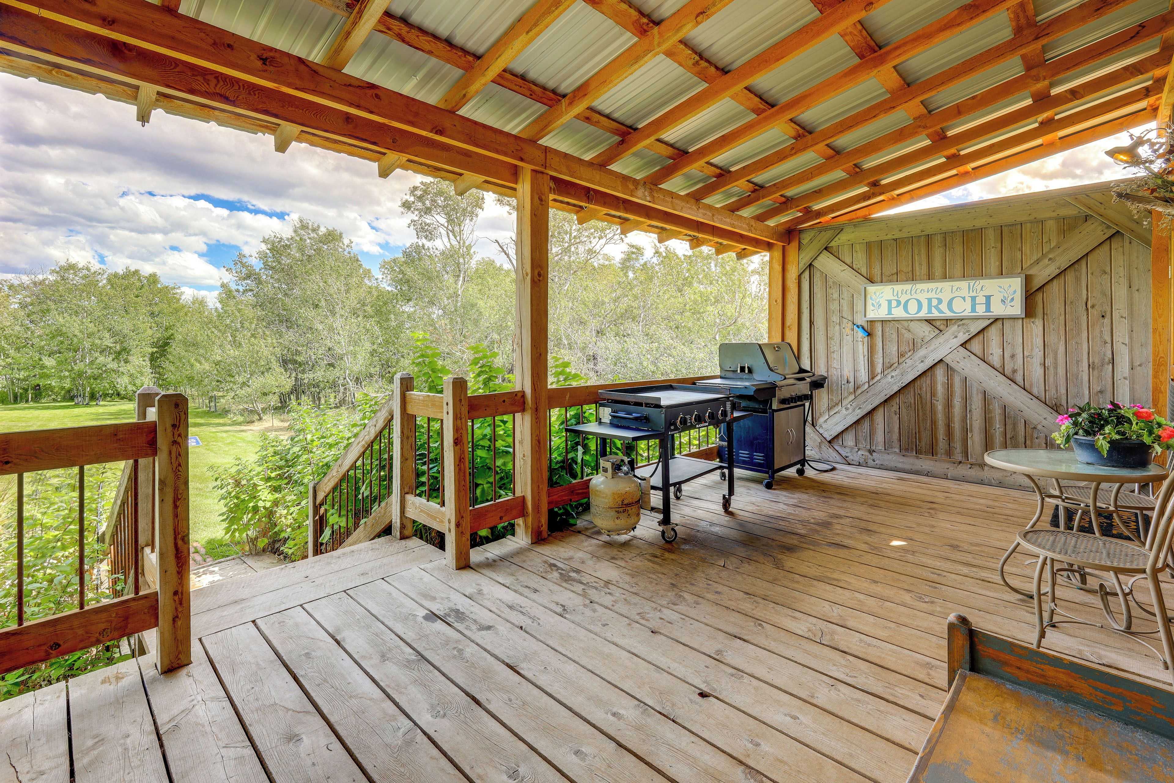 A covered outdoor area with a barbecue grill, a welcome sign, and a table with chairs.