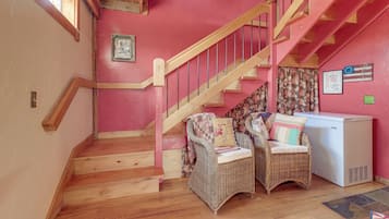 A staircase with wooden steps and a wooden handrail, leading to a landing with wicker furniture and a white appliance.
