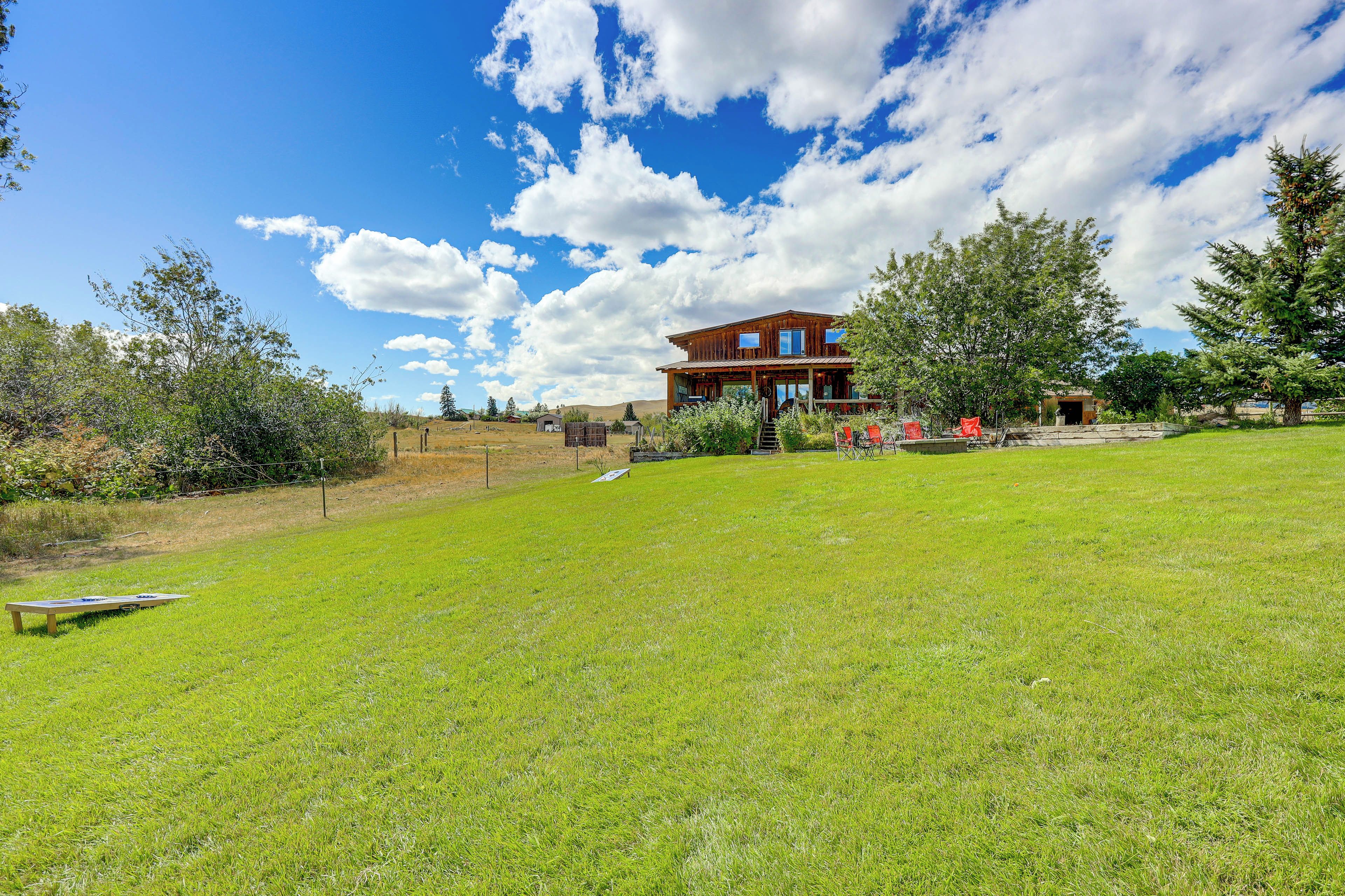 A two-story wooden house with a large lawn, a wooden deck, and a mountain backdrop.