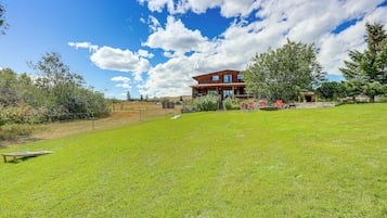 A two-story wooden house with a large lawn, a wooden deck, and a mountain backdrop.