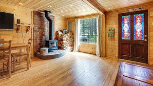 Een gezellig chaletinterieur met een open haard, houten wanden, een eethoek en een groot raam met uitzicht op het bos.