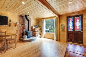 Ein gemütliches Blockhaus-Interieur mit Kamin, Holzwänden, einer Essecke und einem großen Fenster mit Blick auf den Wald.
