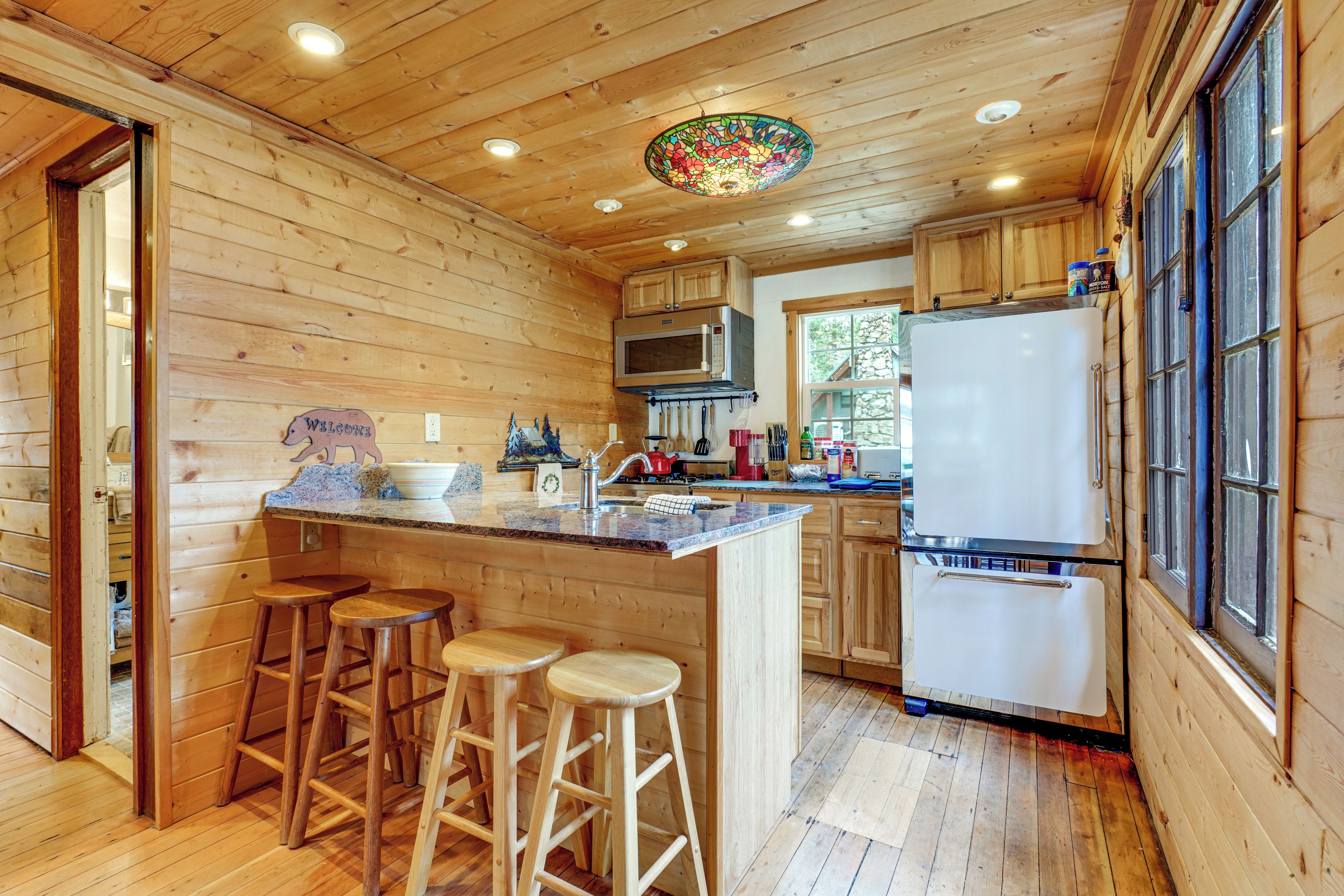 Interior de una cabaña de madera con cocina, que incluye refrigerador, estufa y taburetes de bar.