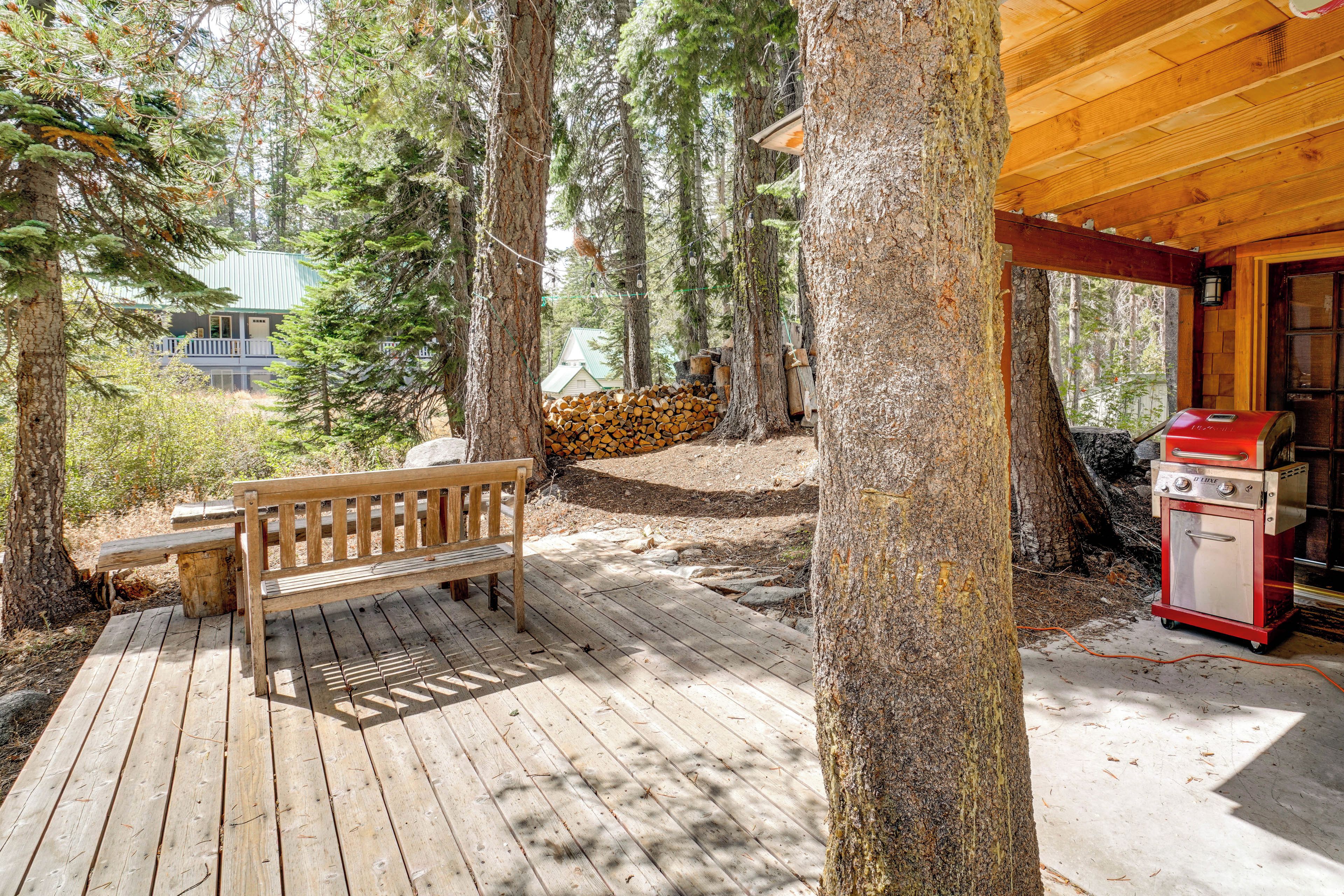 A wooden deck with a bench, a barbecue grill, and a building in the background.